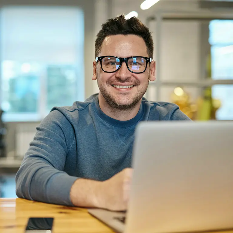 Mann mit Brille lächelt am Schreibtisch, arbeitet an einem Laptop zur SEO-Optimierung von SELTENLY.
