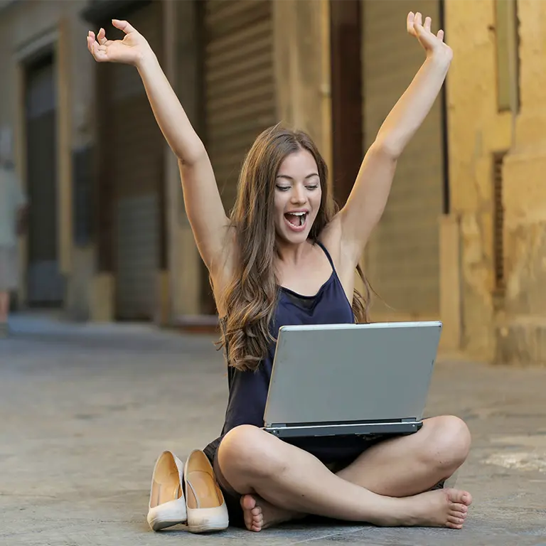 Eine Frau sitzt am Boden mit hochgestreckten Armen, strahlt Begeisterung und Lebensfreude aus.